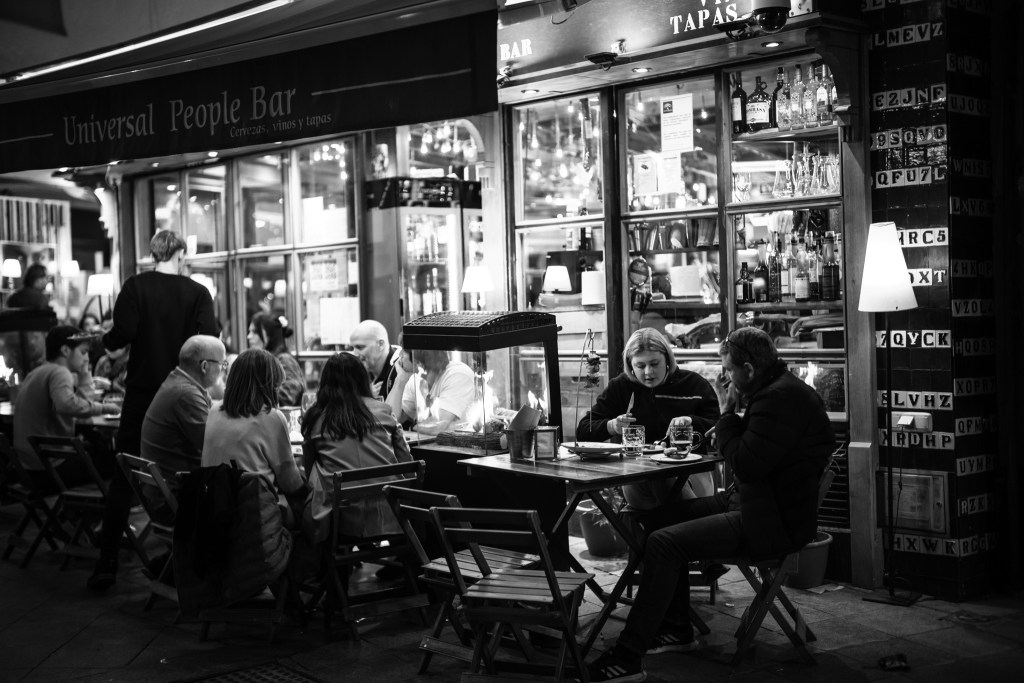 Patrons sitting in front of a bar during a night in Sevilla - Street Photograph by Marcus Puschmann Nuremberg