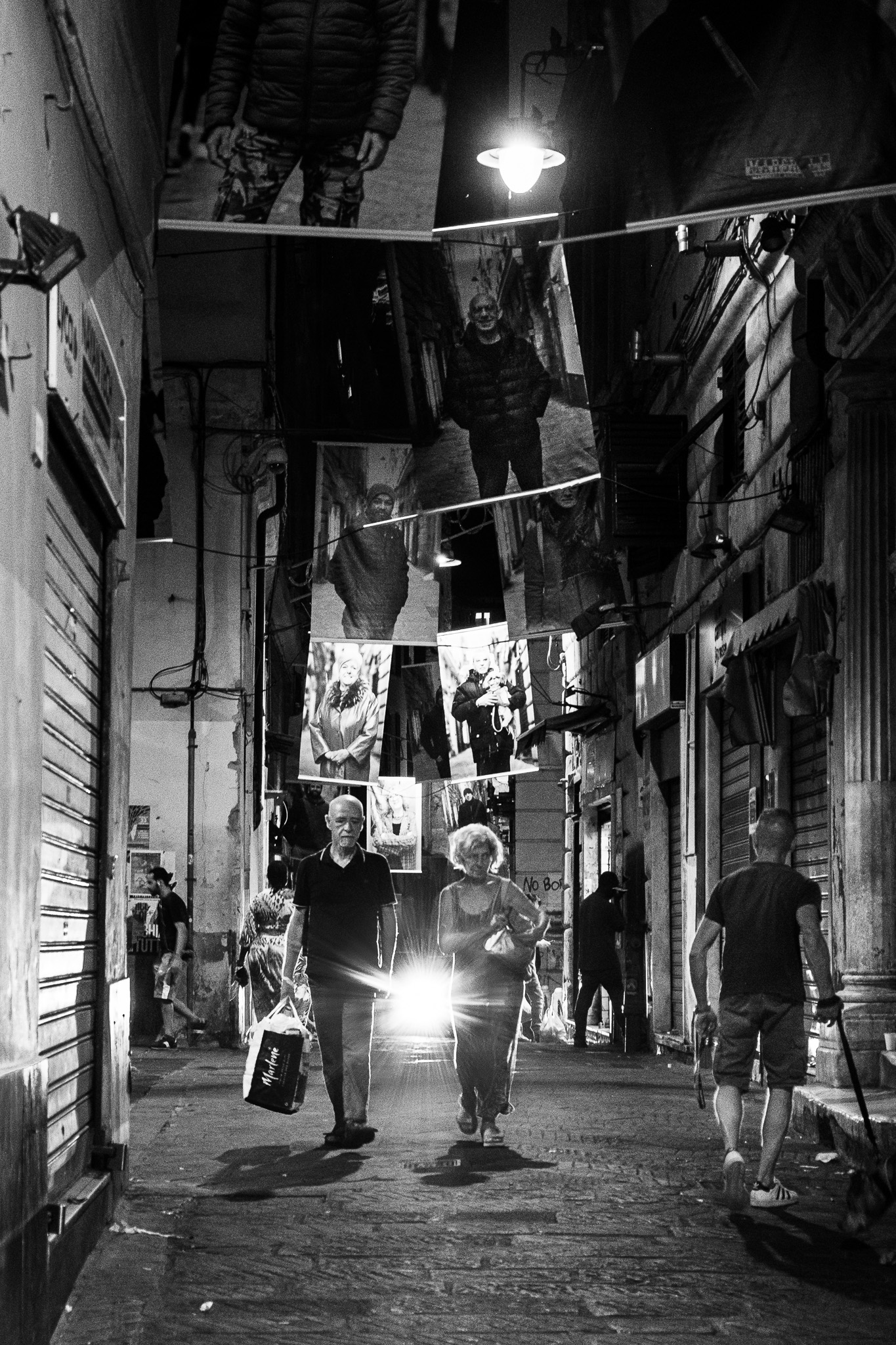 Couple walking side by side through Genoa's Via Pré by night, backlit by an approaching car.