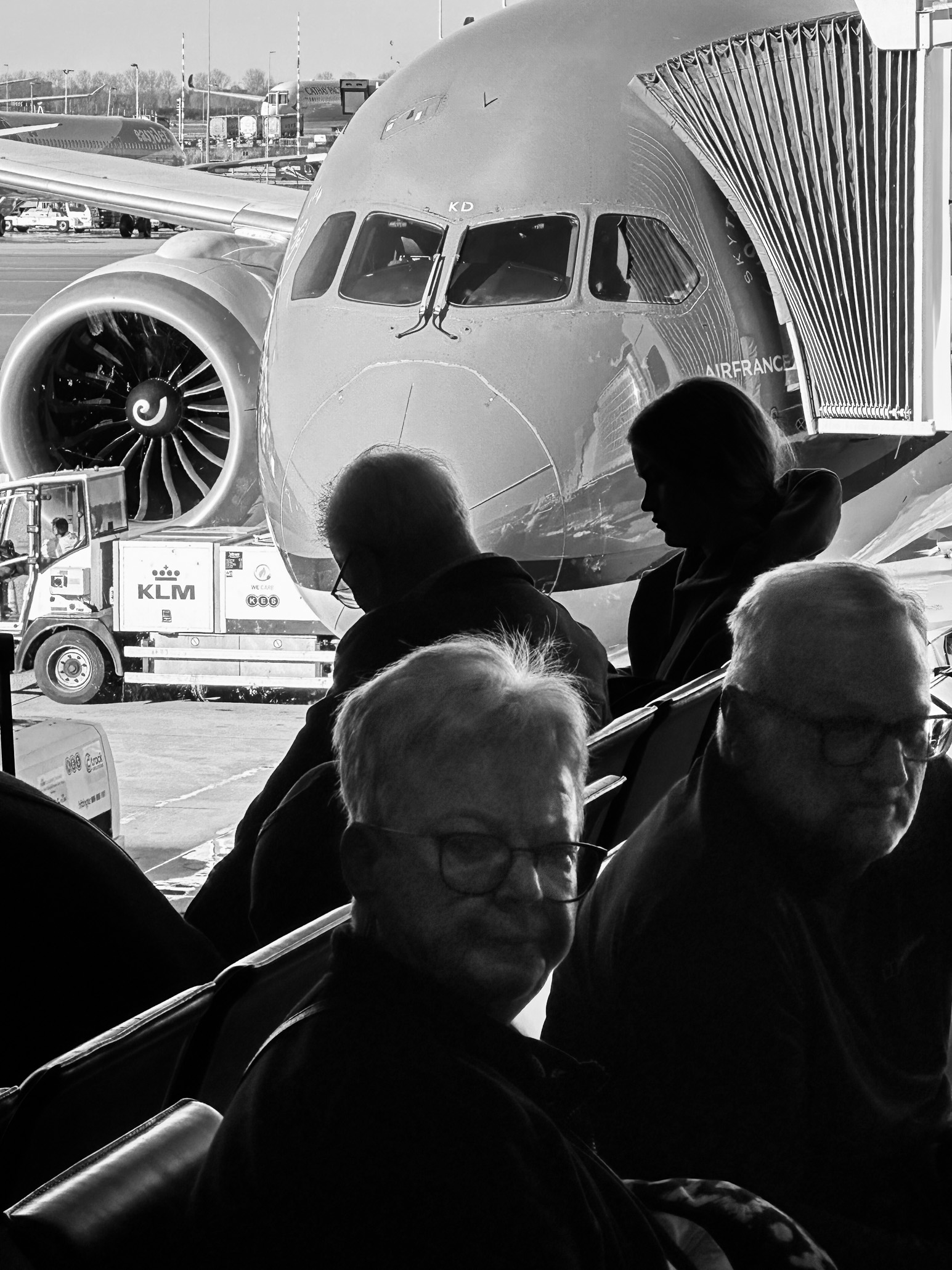 People sitting at an airport window on front of a plane on a travel day