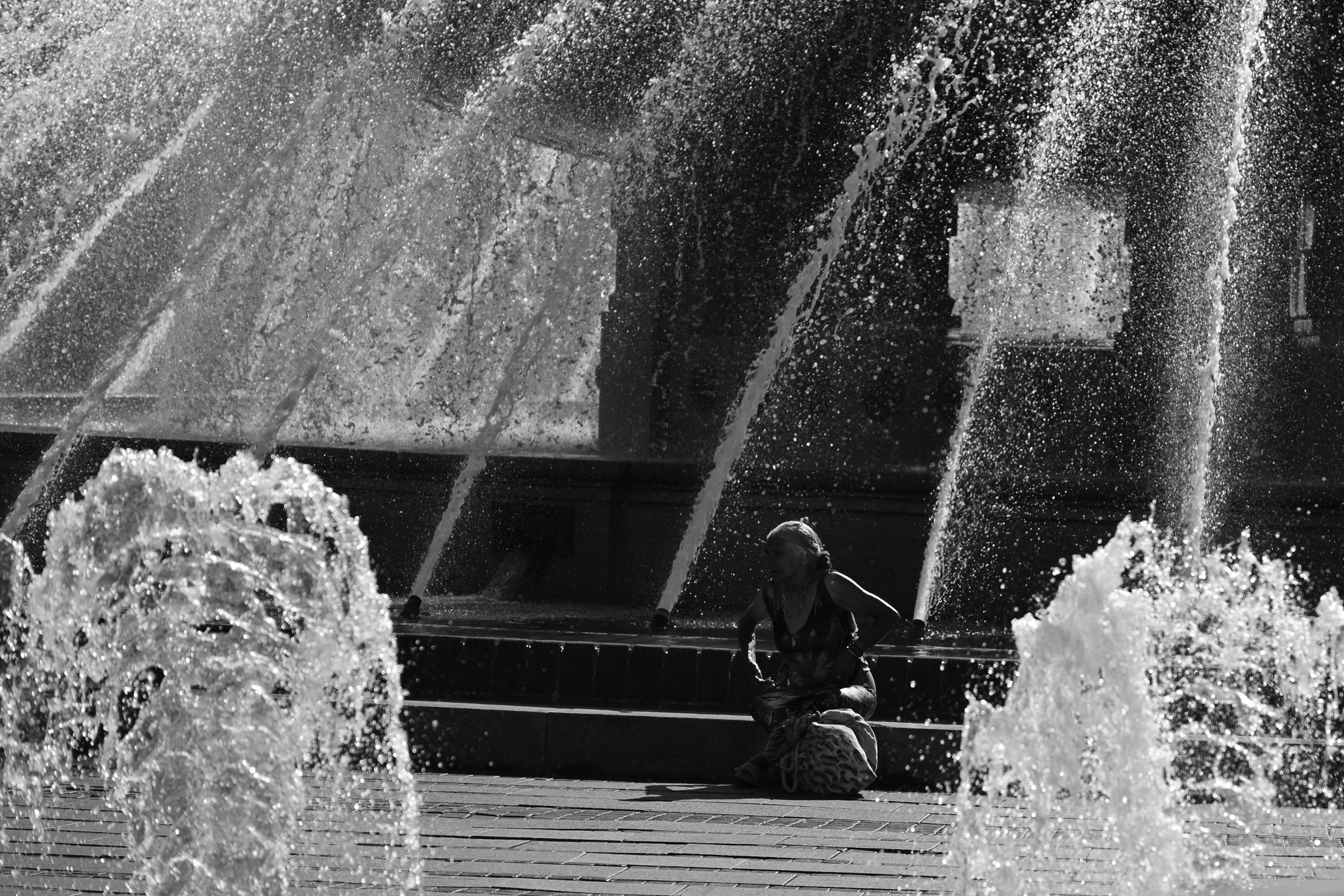 The silhouette of a lady in front of a fountain, enjoying the summer in the city
