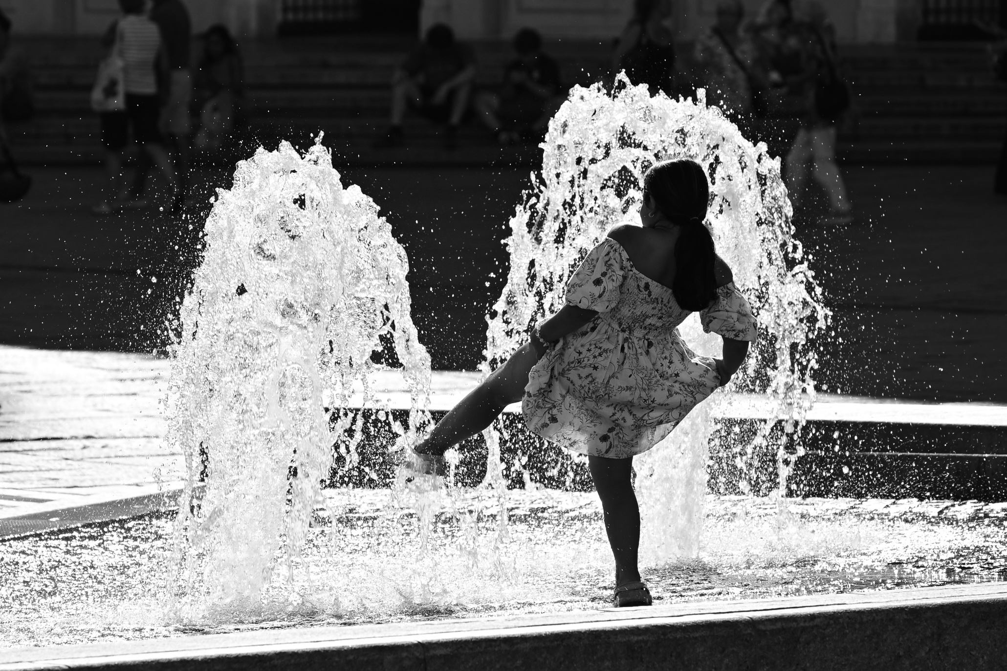 The silhouette of a girl in front of a fountain, enjoying the summer in the city