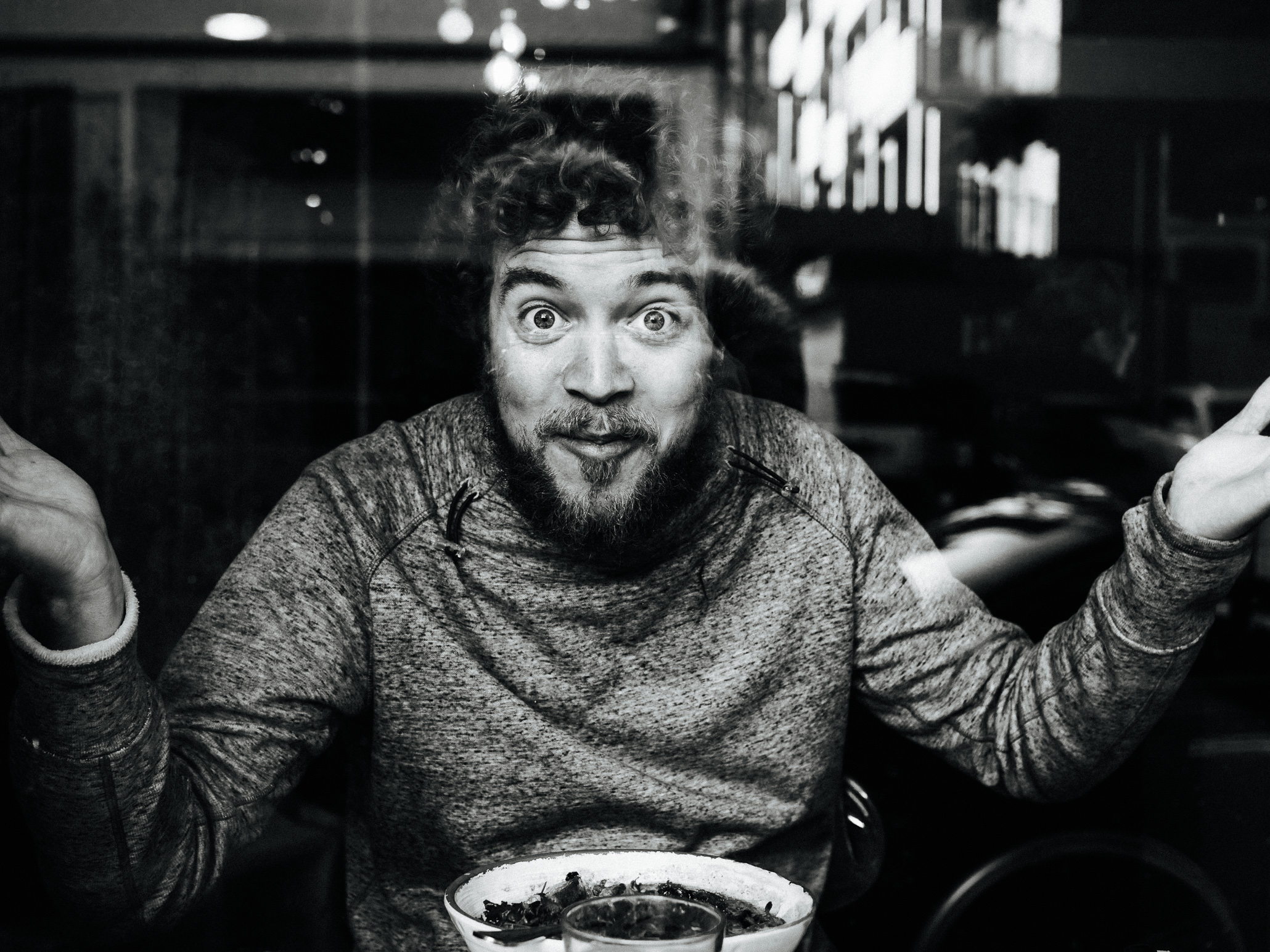 Man eating in a restaurant looking at the photographer through the window making a funny face