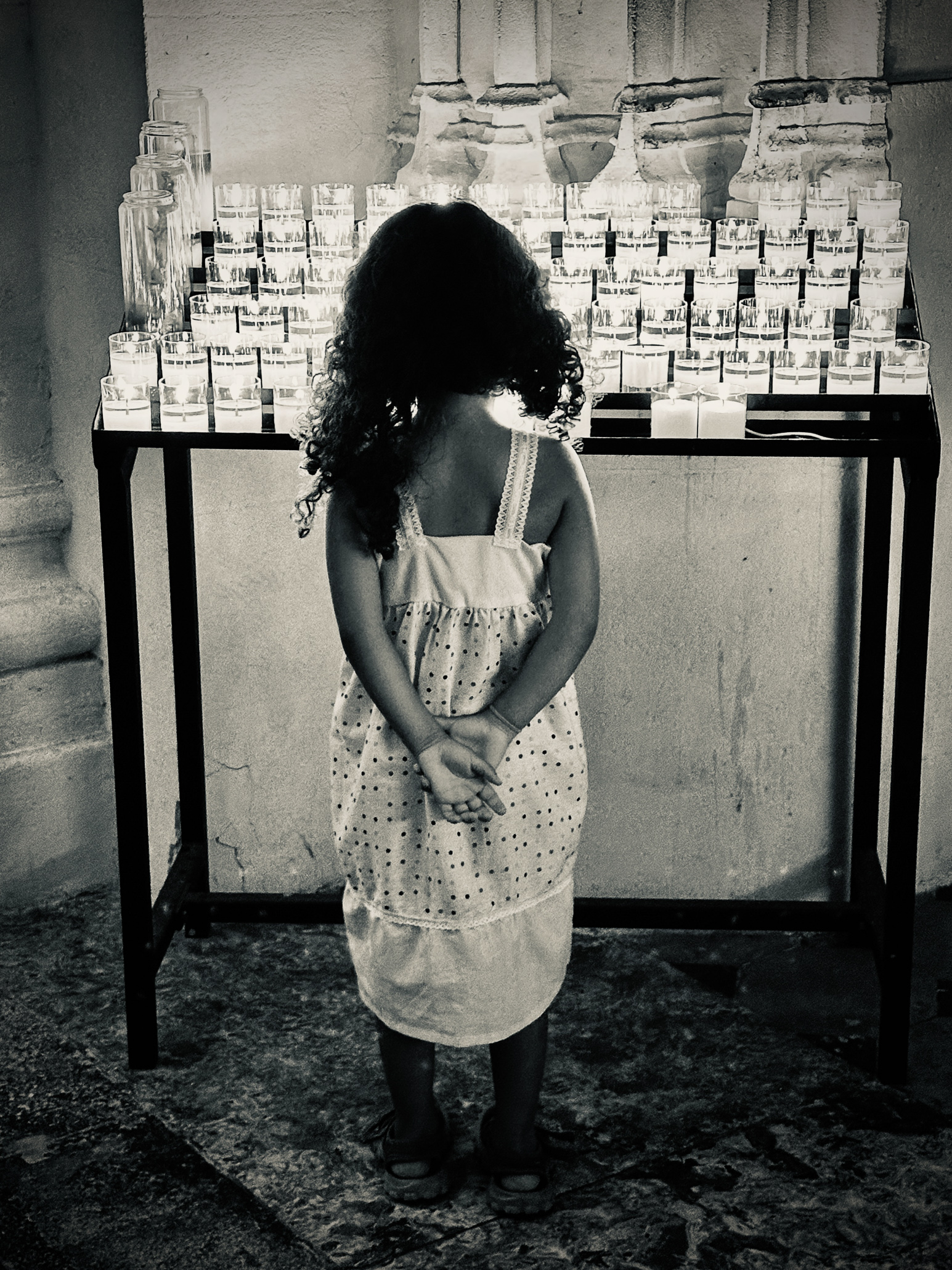 Little girl looking at votive candles in a church, thinking about the wishes behind.