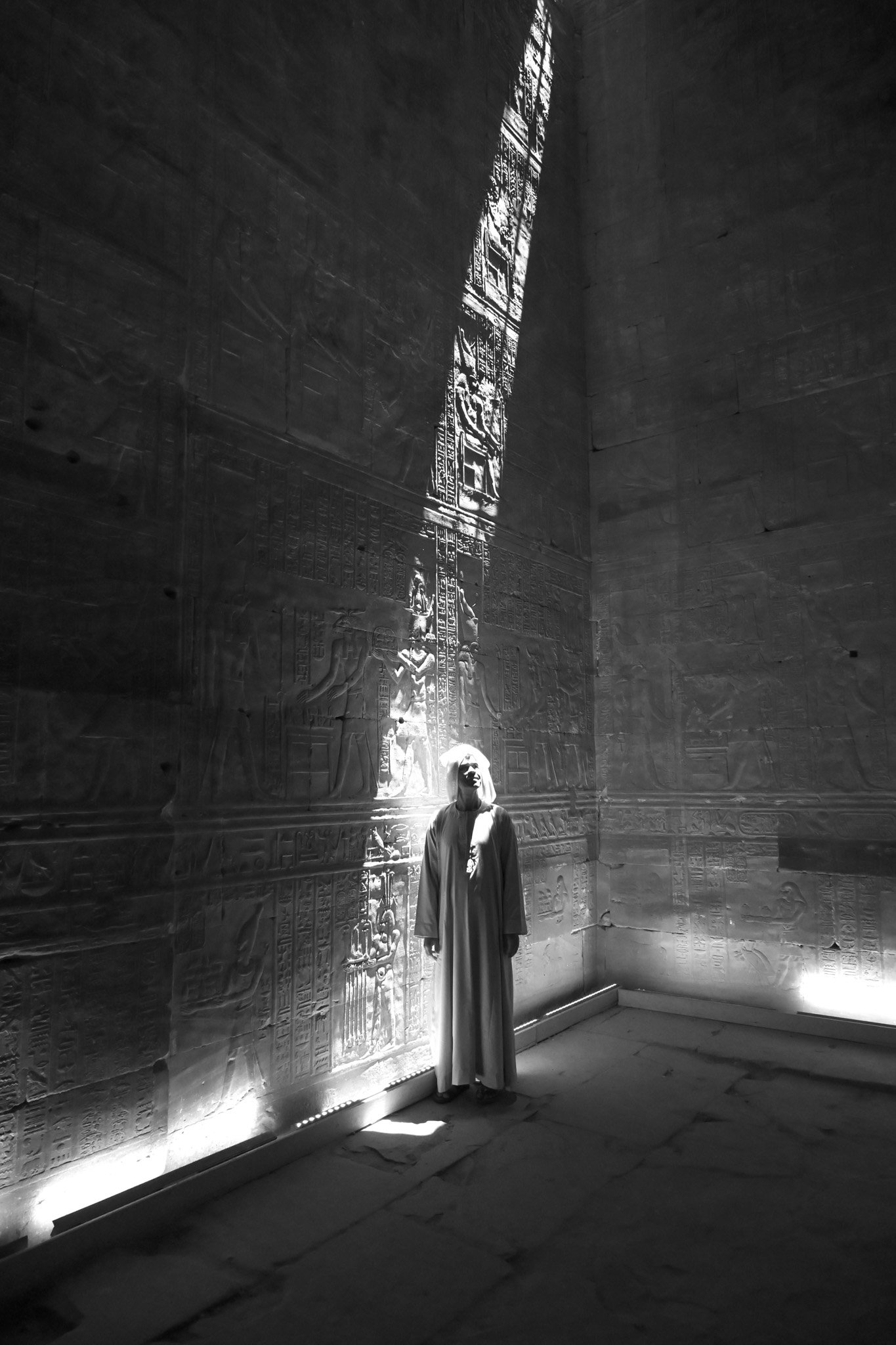 A guardian in an ancient Egyptian temple standing in a shaft of light in front of a wall full of hieroglyphs