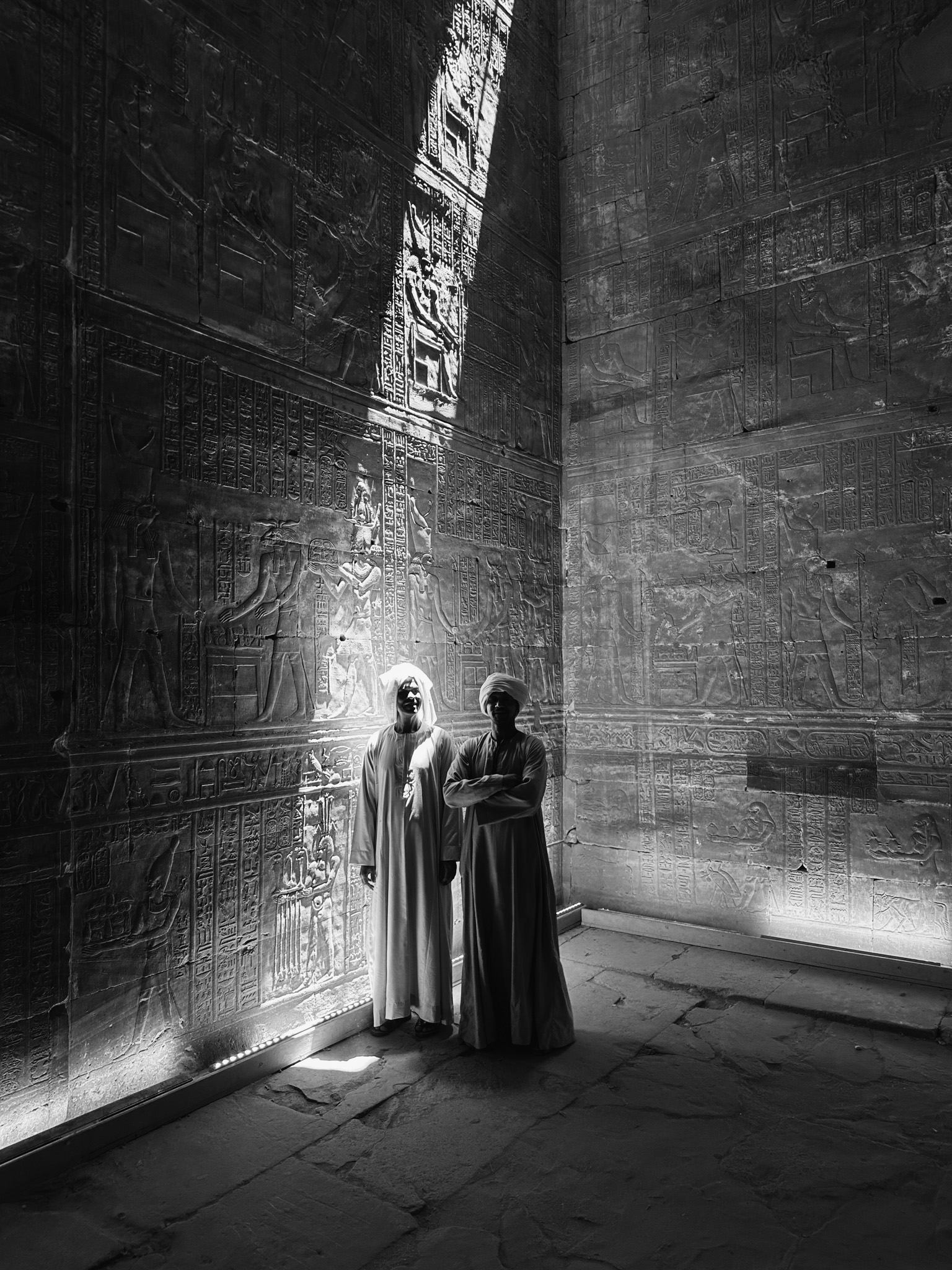 Guardians in an ancient Egyptian temple standing in a shaft of light in front of a wall full of hieroglyphs