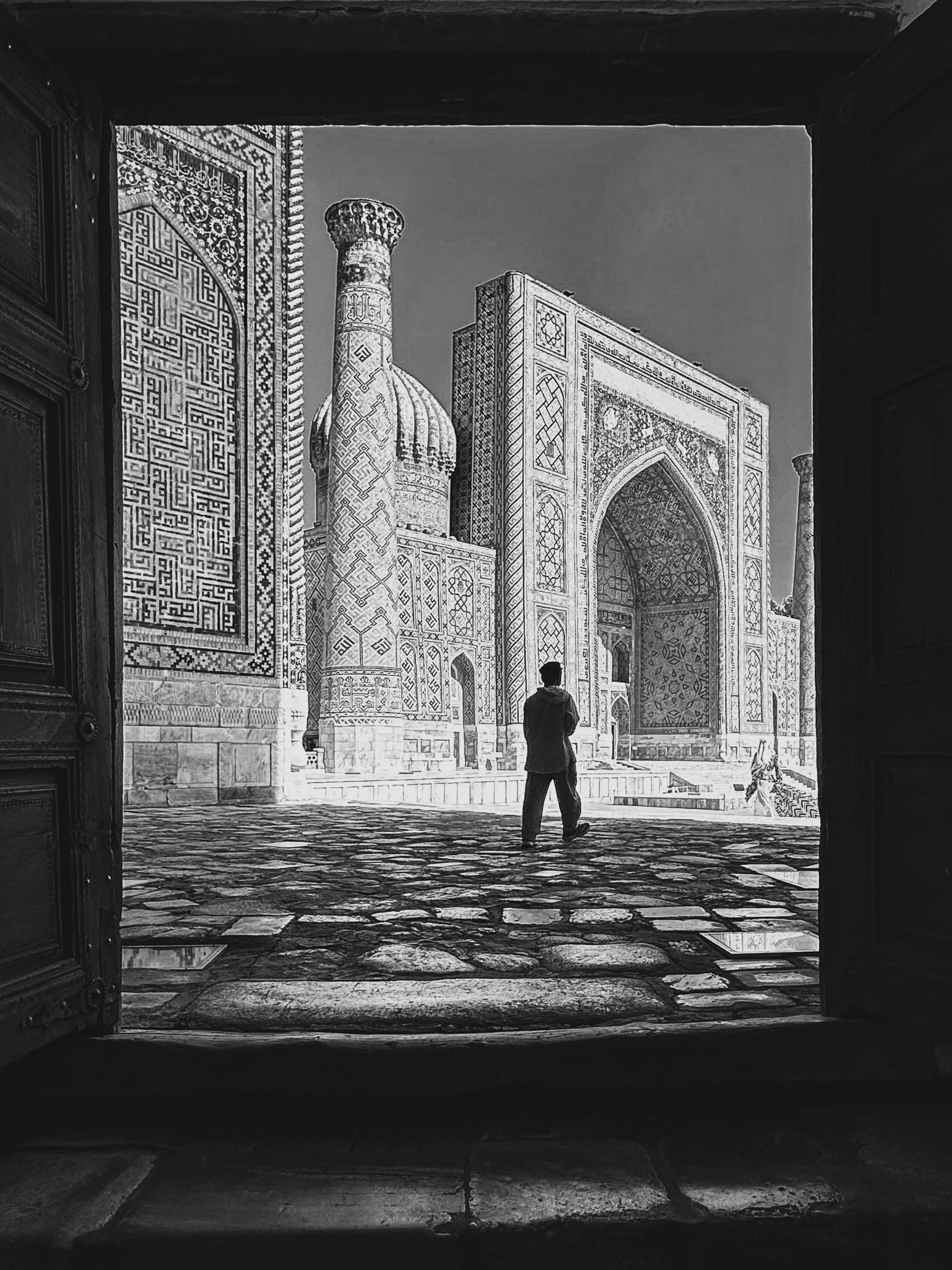 A man walking through a door into the beautiful historic courtyard of a mosque in Samarkand, Uzbekistan.