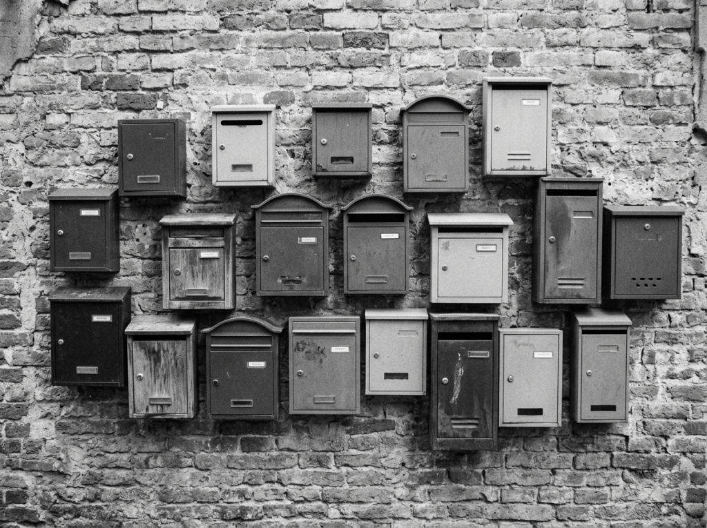 Various vintage mailboxes attached to a weathered brick wall in black and white